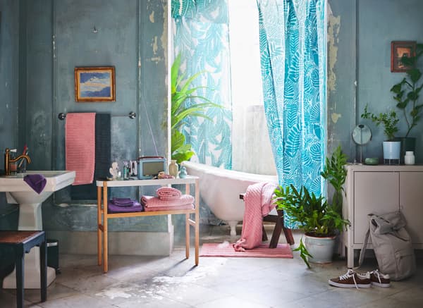 A retro style bathroom setting featuring a white bath with tropical turquoise printed shower curtains and light pink towels.