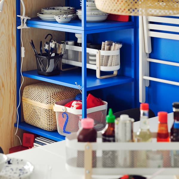 A RISATORP desk organiser with condiments in it is on top of a gateleg table close to a blue PLATSA open shelving unit.