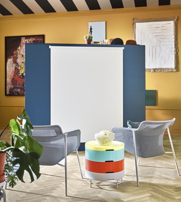 A roller blind attached to a stand-alone wall is pulled down for movie viewing.