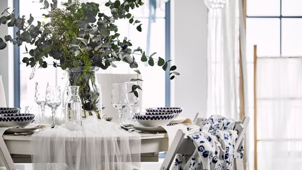 A romantic table setting with white tulle draped over a round table and a vase with wild flowers and eucalyptus leaves.
