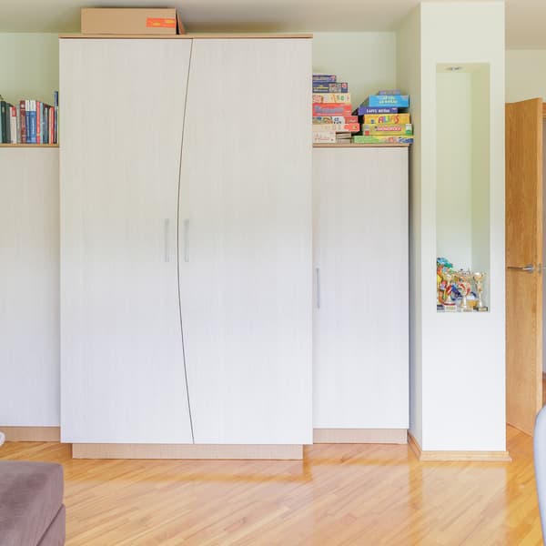 A room before the makeover showing a white wardrobe along one wall, with some items stored on the shelves and a wooden floor.