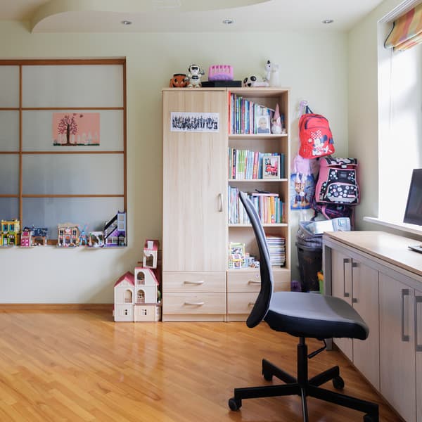 A room before the makeover with a cabinet and office chair placed along the window. Shelves are filled with various items, and the space feels organised but needs updating.