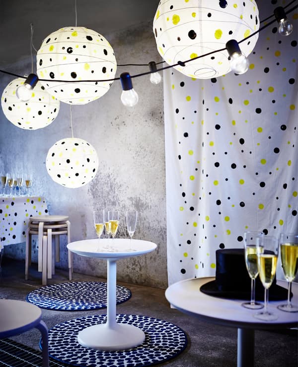 A room decorated with white polka-dotted paper lanterns, string lights, white circular tables, stools and dotted rugs.