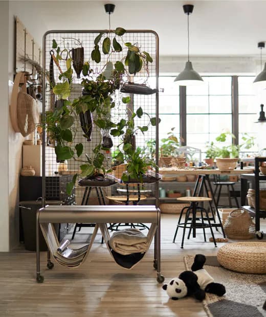 A room divider covered in plants seperates a workspace from a play area in a bright room with black, steel and blonde wood decor.