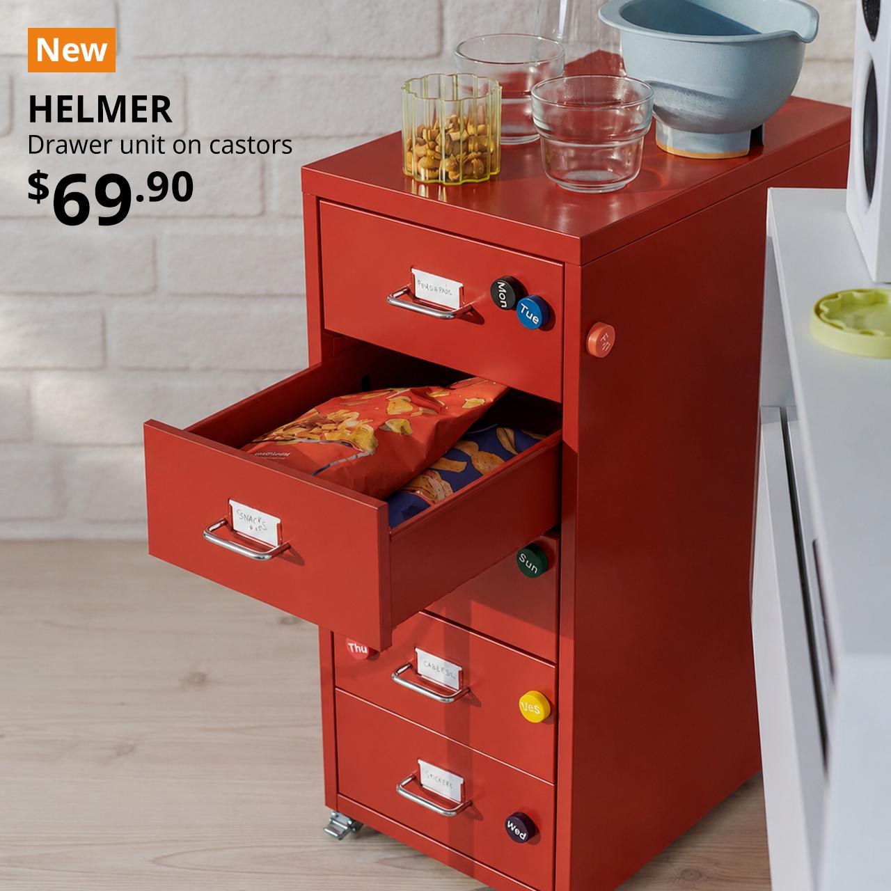 A room features a red HELMER drawer unit on castors, with four drawers filled with snacks, beside a modern chair.