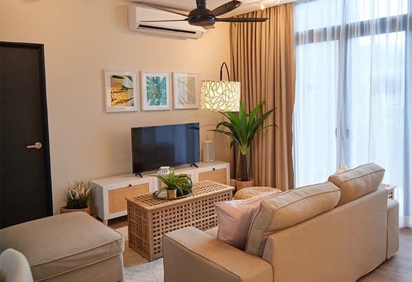A room setting featuirng a sofa, a chest of drawer with a television on top and a woven coffee table.