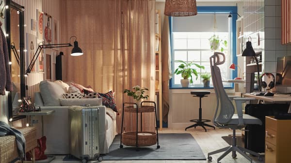 A room with a cart table standing on a rug in front of a HYLTARP sofa bed near a LIDKULLEN active sit/stand support.