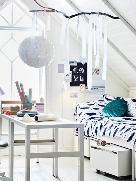 A room with a sloping ceiling and a large window. Two PÅHL desks stand in the middle near two beds and some TROFAST storage.