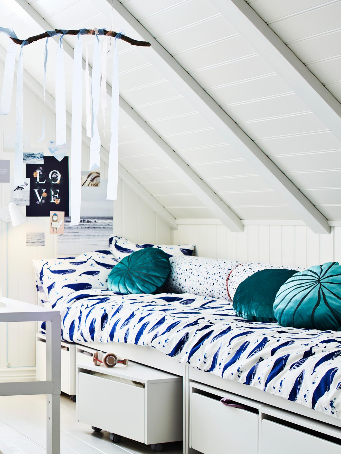 A room with a sloping ceiling where two SLÄKT beds with BLÅVINGAD bed linen stand end to end along one side.