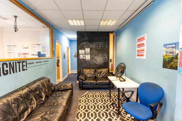A room with blue walls, a black leather sofas, blue desk chair, patterned rug in grey and white.