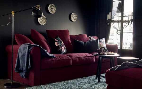 A room with cushions on a sofa, lamp, tables and wall decorations.