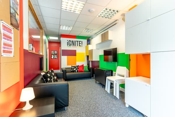 A room with orange walls, white storage cabinets, grey floors and black sofas.