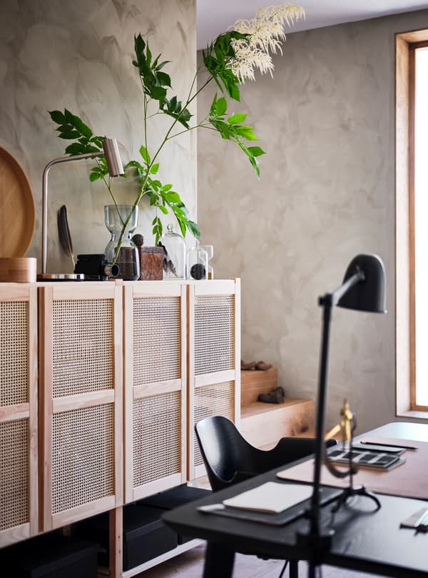 A room with window and lattice-front wall storage unit with a plant and accessories on it and black desk, chair and lamp.