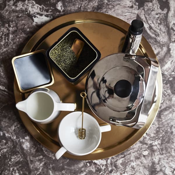 A round gold tray with kettle, mug, milk jug and loose leaf tea inside a container.