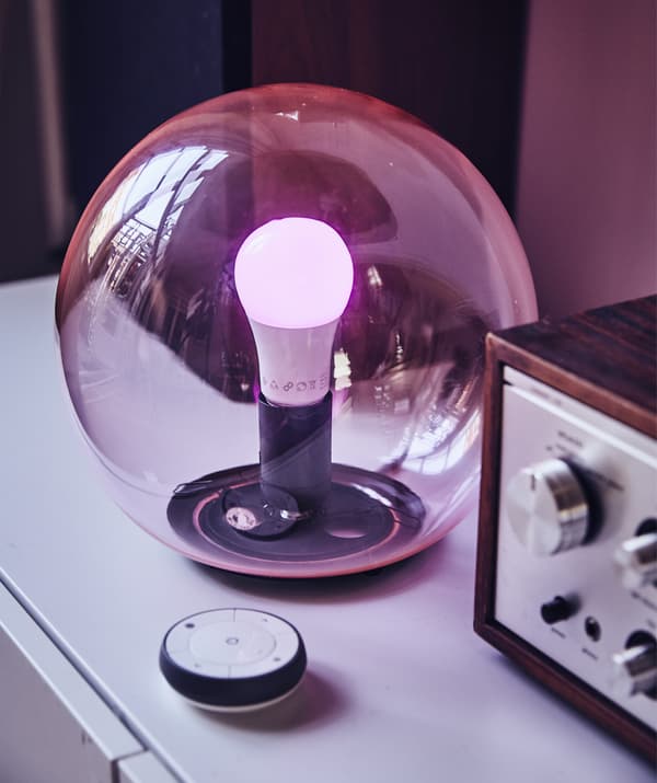 A round, see-through pink glass table lamp with a remote.