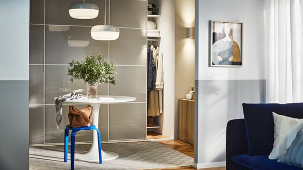 A round table and a blue KYRRE stool in a hallway, in front of a storage combination with SKYTTA/HOKKSUND sliding doors.