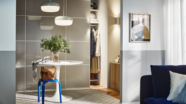 A round table and a blue KYRRE stool in a hallway, in front of a storage combination with SKYTTA/HOKKSUND sliding doors.