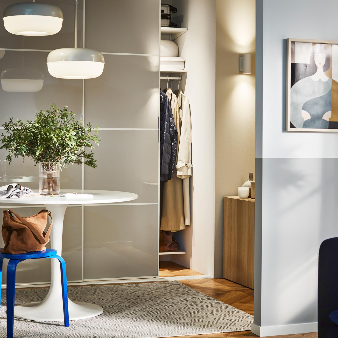 A round table and a blue KYRRE stool in a hallway, in front of a storage combination with SKYTTA/HOKKSUND sliding doors.