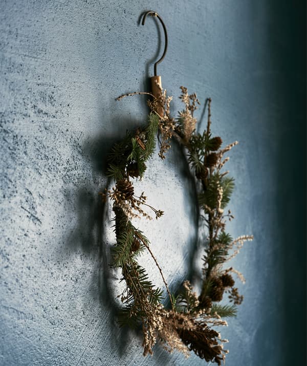 A round, thin winter wreath made from pine cones and woodland branches, hanging on a dark blue wall.