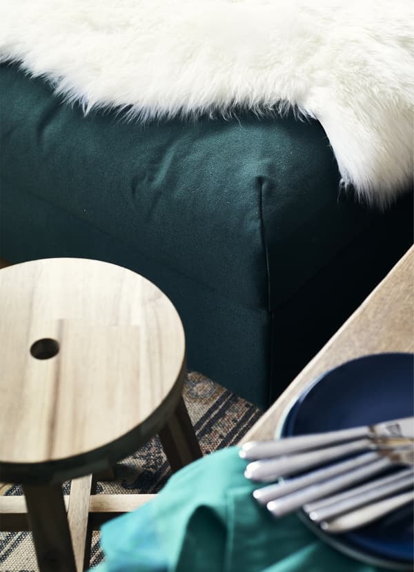 A round wooden stool and a sheepskin rug on a green footstool.