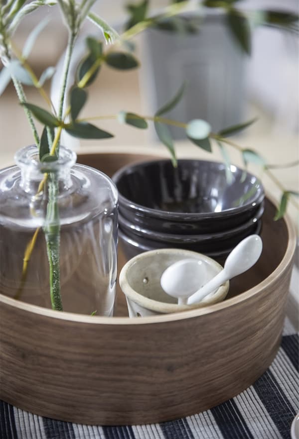 A round wooden tray containing bowls and a vase with eucalyptus.