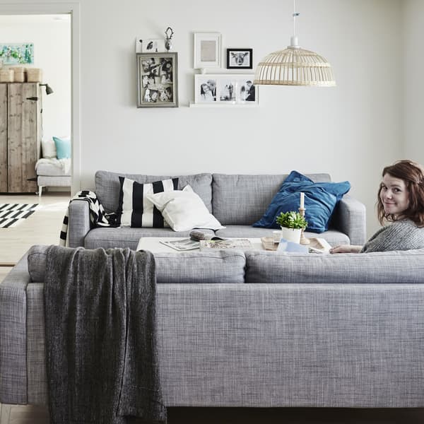 A rustic living space with a woman sitting on sofa with throws and cushions.