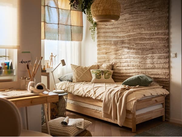 A rustic-style room with a pine UTÅKER stackable bed covered in NYPONLUGGMAL bed linen by a wall with a textured rug on it.