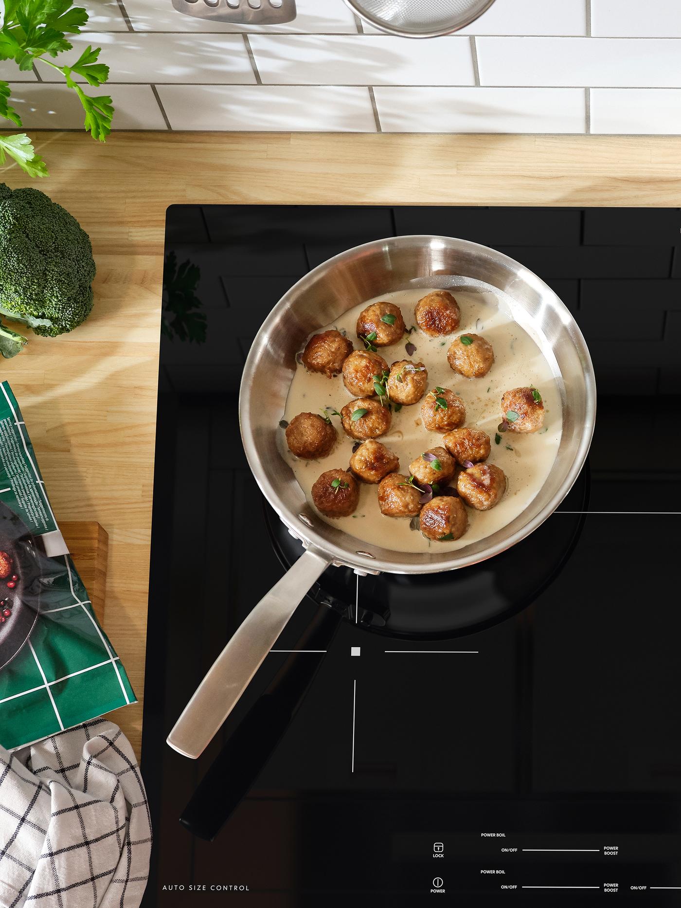 A sauté pan with meatballs and sauce inside stands on a black induction hob.