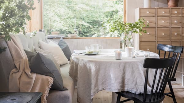 A Scandinavian-style dining area with lit ADLAD scented candles and tealights on top of a dining table, by a large window.