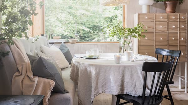 A Scandinavian-style dining area with lit ADLAD scented candles and tealights on top of a dining table, by a large window.