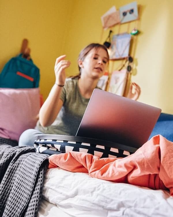A schoolchild studies on her computer while sat on her bed, the laptop held steady by a BYLLAN laptop support.