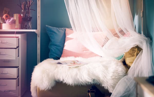 A seating area with sheepskin rug, various cushions and a voile curtain.