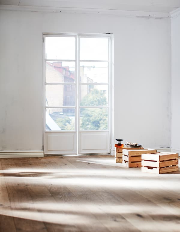 A section of a sunny empty room with a white, unpainted wall and floor in natural wood.