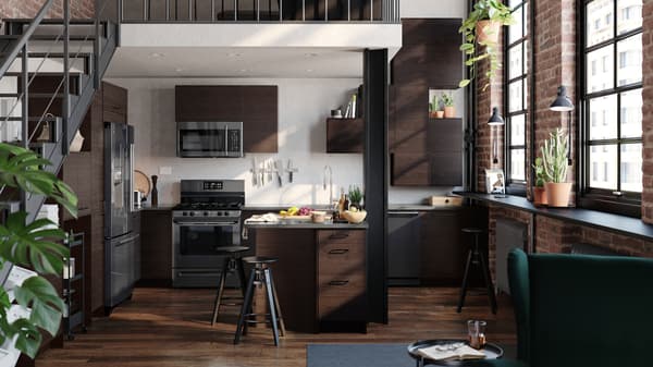 A SEKTION kitchen in dark brown, with stairs to the side and a landing above, windows to the right, plants in the windowsill.