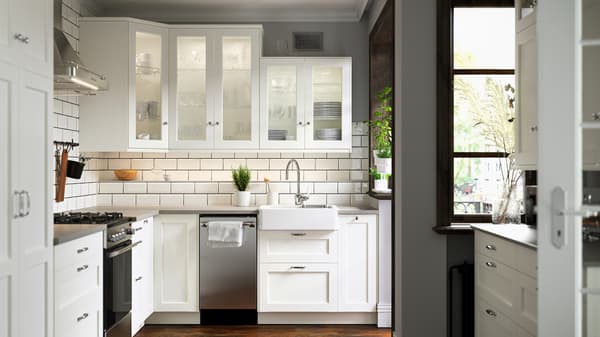 A SEKTION kitchen with white tiled walls and ENKÖPING fronts, plants on the windowsill and worktop, and white wall cabinets.