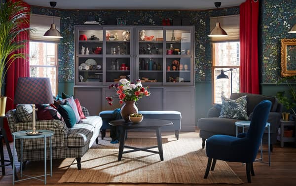 A set of soft seating including a plaid sofa and blue chair and bench, in a room with gray cabinets and floral wallpaper.