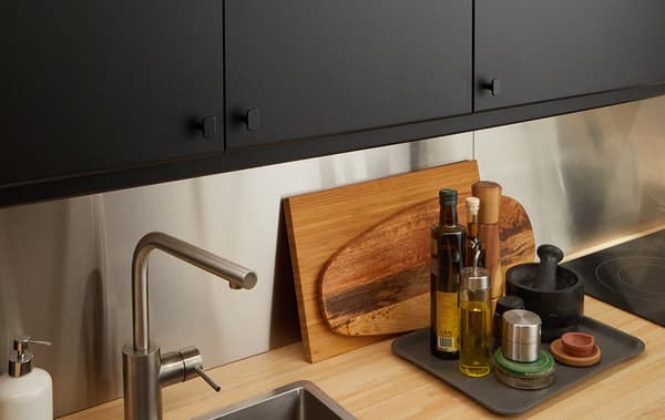 A set of upper kitchen cabinets mixed with open shelving and black doors, a wood countertop below with a sink and faucet.