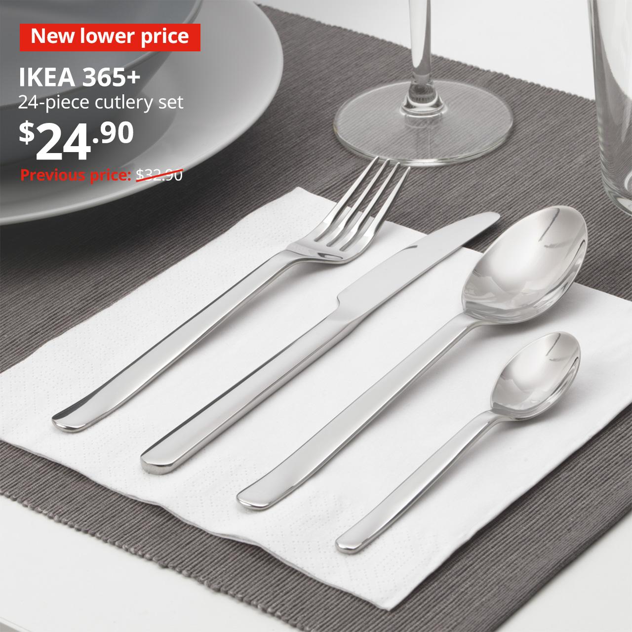 A set out of the 24-piece stainless steel IKEA 365+ cutlery is being placed on a white FANTASTISK napkin on a dining table setting. Image with New lower price tag. Price: $24.90. Usual price with red slash: $32.90.