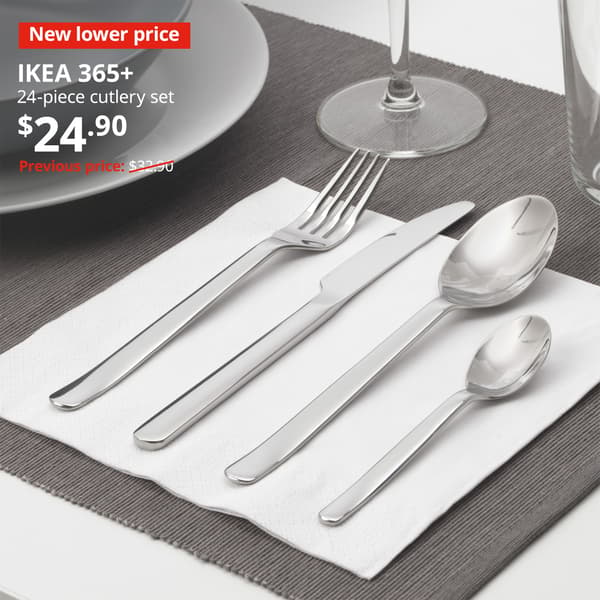 A set out of the 24-piece stainless steel IKEA 365+ cutlery is being placed on a white FANTASTISK napkin on a dining table setting. Image with New lower price tag. Price: $24.90. Usual price with red slash: $32.90.