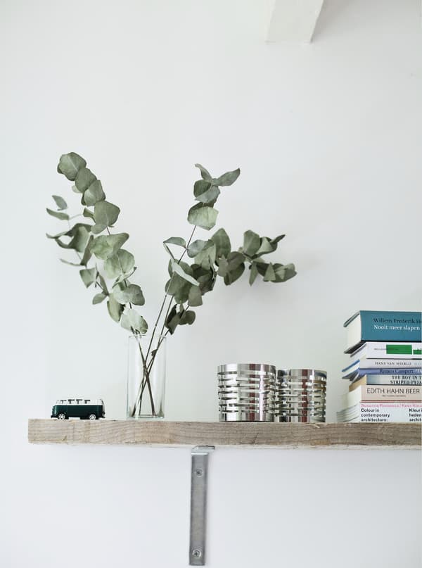 A shelf with a glass vase, decorative pots and books.