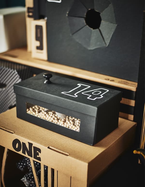 A shoe box filled with dried peas visible through a plastic cut-out window.