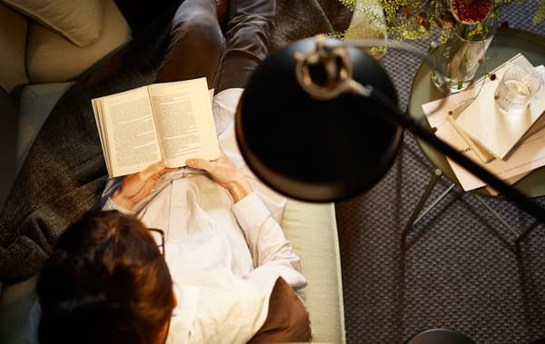 A shot from above of a lamp lighting a woman while she’s reading on the sofa.