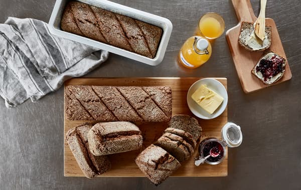 A shot from above of a table with prepared loaves of bread, butter, jam and orange juice.