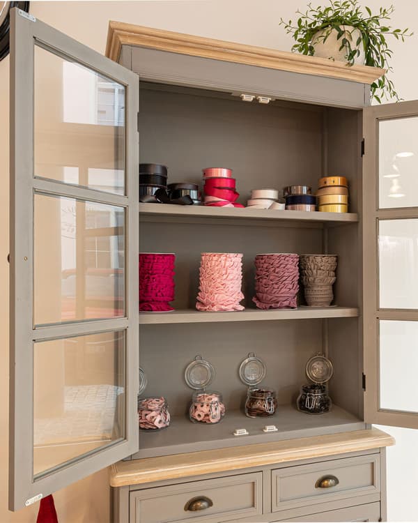 A showcase with open glass doors with various ribbons and yarn spools.