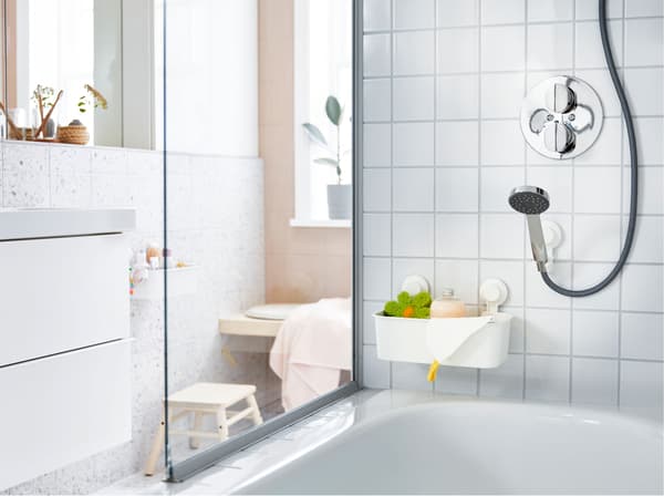 A shower head, above a bath, in a white tiled bathroom, held with an adjustable bracket and suction cup.