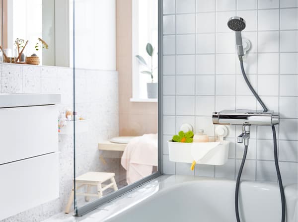A shower head, above a bath, in a white tiled bathroom, held with an adjustable bracket and suction cup.