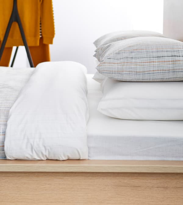 A sideview of a neatly made bed with white linens and simple striped pillows.