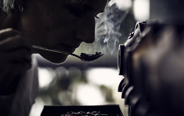A silhouette of a person smelling coffee beans on a spoon.
