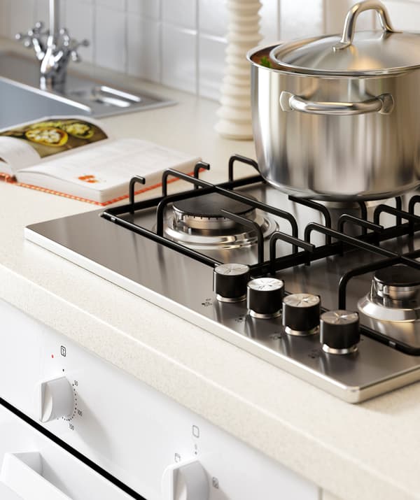 A silver pot on a hob on a white kitchen worktop next to a metal sink.