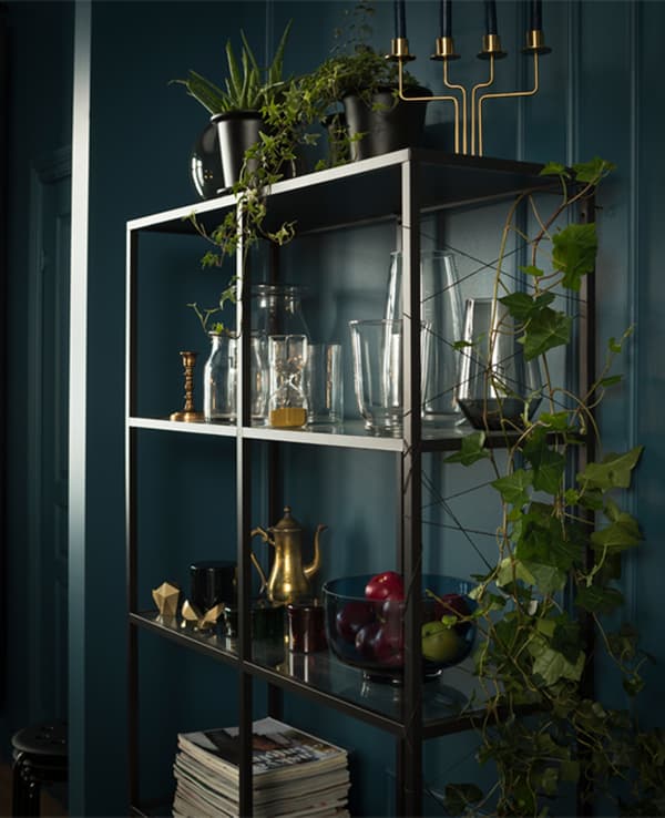 A simple black shelving unit displays glass vases and other decorative items, while twine crisscrossing the side serves as a trellis for a climbing plant.